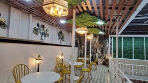 Een restaurant met ronde tafels en gele stoelen, een betegelde vloer en een groene wand met planten.