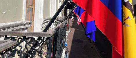 A building facade with a balcony railing, a flag, and a clear sky.
