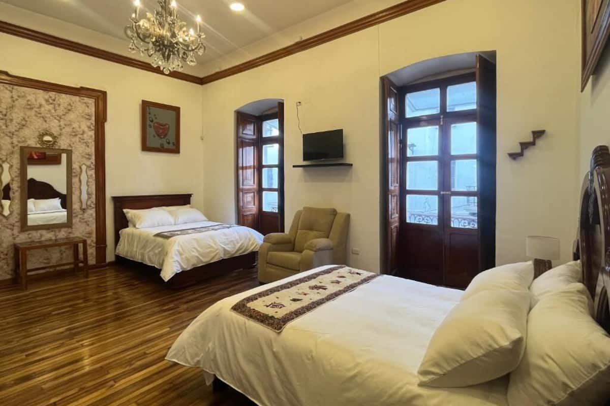 Habitación de hotel con dos camas, un candelabro, un televisor y un ventanal grande.