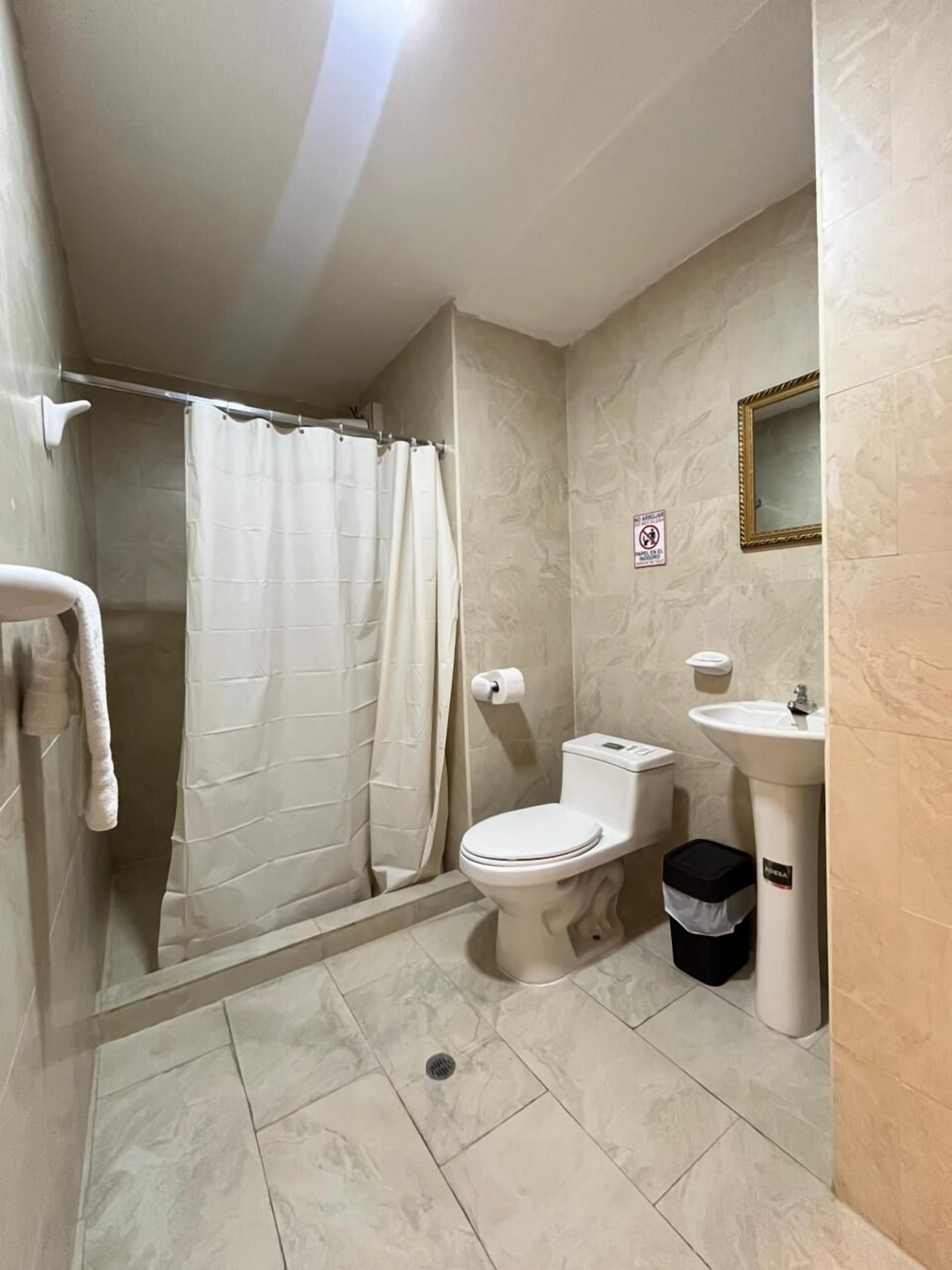 Une salle de bain équipée d’une douche, de toilettes, d’un lavabo et d’une poubelle.