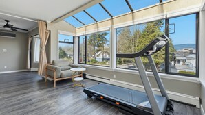 A spacious room with a treadmill, large windows, and a view of the outdoors. - Luxury 5BR Point Grey | Jericho Beach + Downtown (Vancouver)