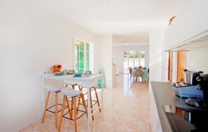 A kitchen with a dining area, a counter with a coffee machine, and a view of the outside. - Amazing home in Cales de Mallorca (Cales de Mallorca)