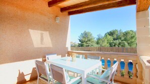 Une terrasse extérieure avec une table et des chaises, un plafond en bois et une vue sur des arbres et une clôture.