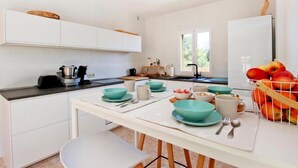 Une cuisine moderne avec des meubles blancs, une table à manger agrémentée de bols turquoise et un panier de fruits.