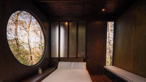 A bedroom with a large round window, a bed with white linens, a bedside table with books, and a bench along the wall. - WANDER CABINS MIneral del Chico (Mineral del Chico)