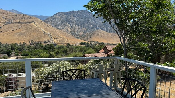 Un balcón con una mesa y sillas, con vistas a un paisaje montañoso y una casa al fondo.
