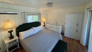 Un dormitorio con cama, mesitas de noche, cuna, armario y ventana.