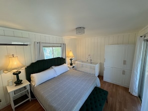 Une chambre à coucher comprenant un lit, des tables de chevet, un berceau, une armoire et une fenêtre.