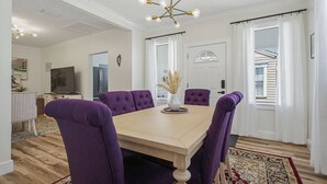 Ein Essbereich mit einem Holztisch, violetten Stühlen, einer Kandelaber und Blick auf einen Raum mit Tür und Vorhängen.