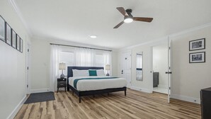 Ein Schlafzimmer mit einem Bett, einem Deckenventilator, einer Tür und einem kleinen Tisch mit Lampe.