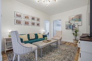Un salon avec un canapé vert, deux fauteuils, une table basse et un tapis à motifs.