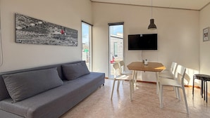 A modern living room with a grey sofa, a wooden dining table with white chairs, a flat-screen TV mounted on the wall, and a large window with a view of the street. - Gorgeous home in Vejen with indoor swimming pool (Vejen)