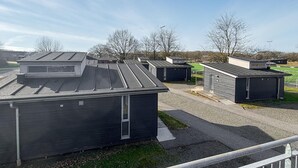 A row of small, dark-colored buildings with flat roofs, arranged in a row on a gravel surface with a grassy field and leafless trees in the background. - Gorgeous home in Vejen with indoor swimming pool (Vejen)