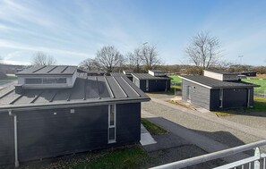 Eine Reihe kleiner, dunkel gefärbter Gebäude mit flachen Dächern, die auf einer Schotterfläche angeordnet sind, mit einem Rasenfeld und kahlen Bäumen im Hintergrund.