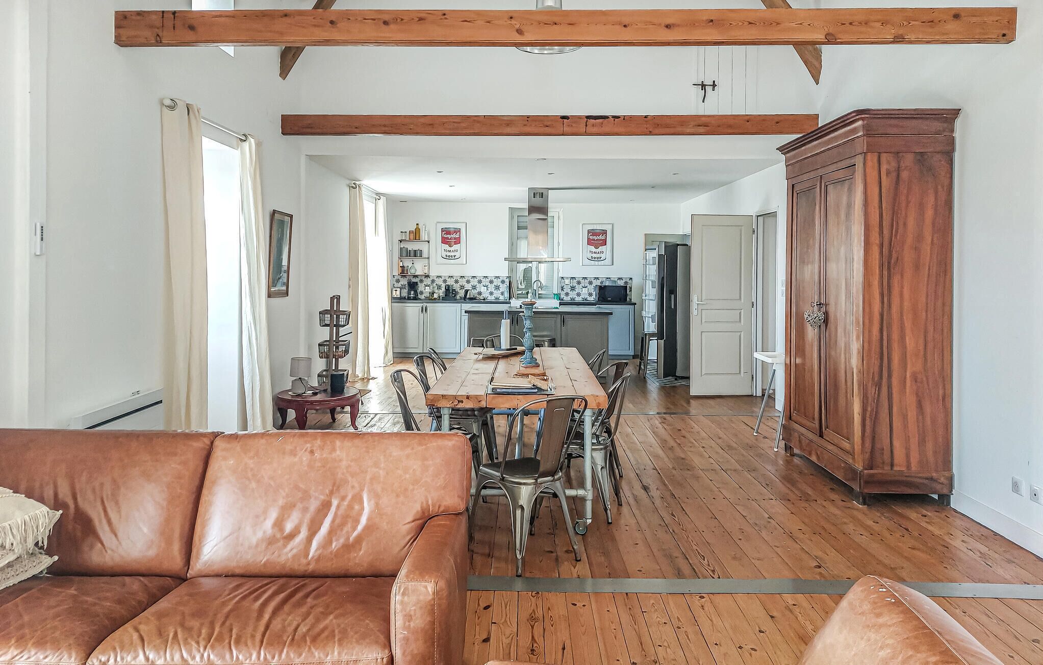 A spacious living area with a wooden dining table, leather sofa, and a large wooden cabinet.