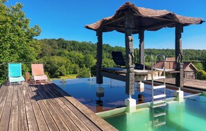 Une terrasse en bois avec une piscine, un kiosque et deux chaises.