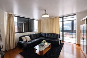 A modern living room with a black leather sectional sofa, a glass coffee table, and large windows with curtains. - Bayview Apartment w/ Outdoor Area, Walk to Beach (Machico)