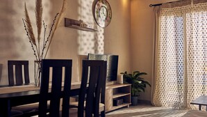 Uma área de refeições com mesa de madeira, cadeiras, televisão e um vaso com planta.