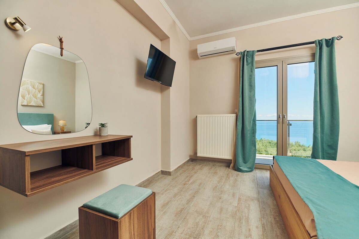 Een slaapkamer met een bed, een televisie, een spiegel, een plank, een bankje, een raam met gordijnen en een radiator.