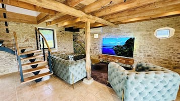 Un vaste espace de vie agrémenté d’un mur en pierre, d’un escalier en bois et d’un grand téléviseur à écran plat.