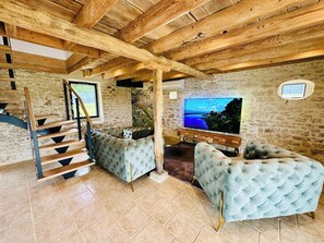 A spacious living area with a stone wall, a wooden staircase, and a large flat-screen TV. - Le Belvédère du Quercy - Domaine Gouloumès (Soucirac)