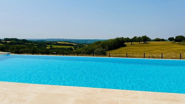 A clear blue swimming pool with a view of a green landscape and hills in the background. - Le Belvédère du Quercy - Domaine Gouloumès (Soucirac)