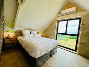 A bedroom with a bed, a nightstand, a lamp, and a large window with a view of the outdoors. - Le Belvédère du Quercy - Domaine Gouloumès (Soucirac)