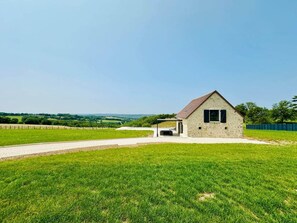 A single-story stone building with a sloped roof, a covered porch, and a paved driveway leading to it. - Le Belvédère du Quercy - Domaine Gouloumès (Soucirac)