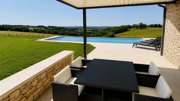 Um pátio ao ar livre com mesa e cadeiras, piscina e vista para uma paisagem verde.