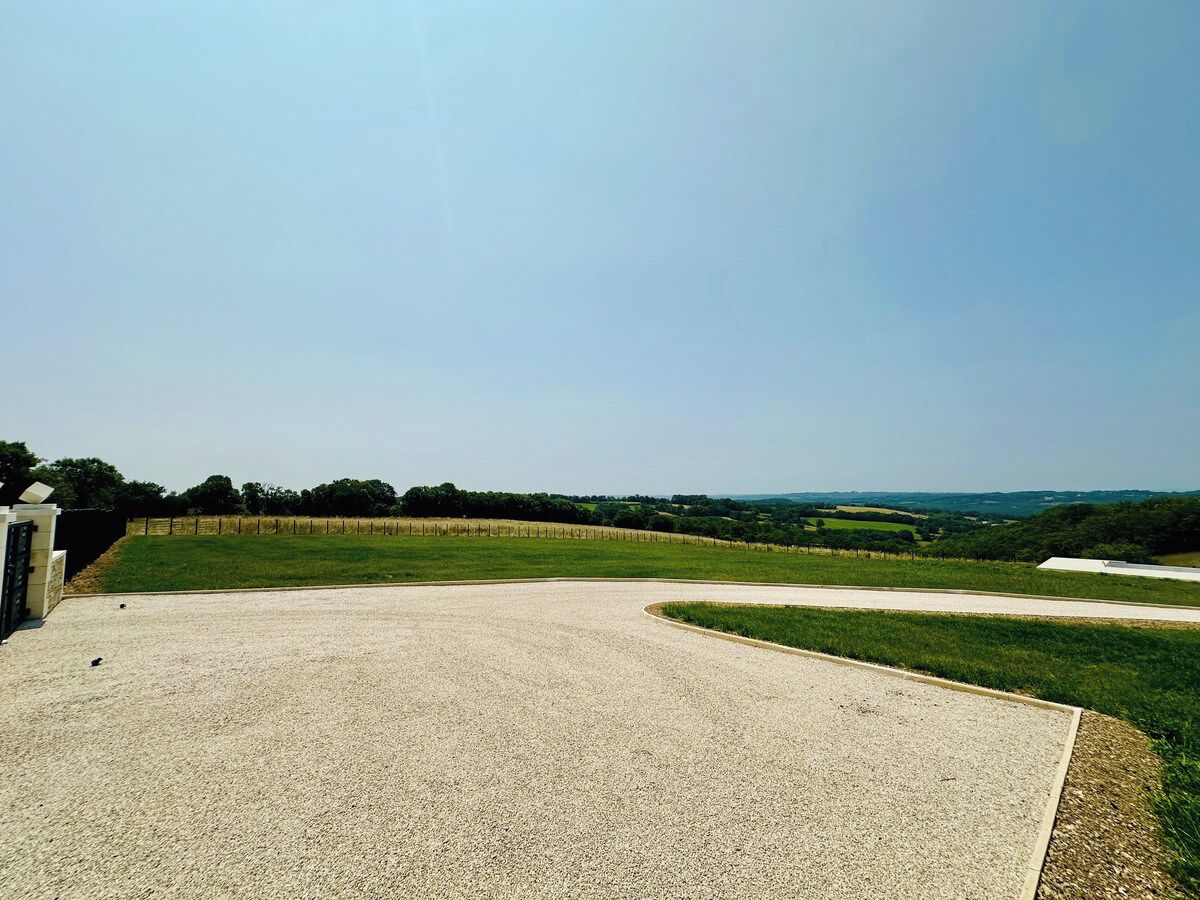 A gravel-covered area with a curved path, surrounded by grassy fields and a fence.
