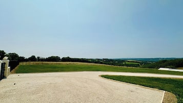 A gravel-covered area with a curved path, surrounded by grassy fields and a fence.