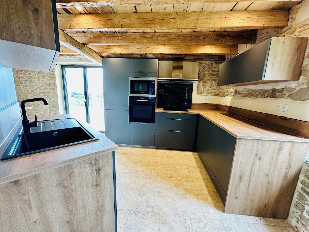 Cozinha moderna com eletrodomésticos embutidos, parede de pedra e teto de madeira.