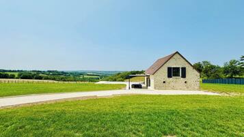 A small stone building with a sloped roof, a covered outdoor seating area, and a paved driveway.