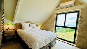 A bedroom with a bed, two bedside lamps, a window with a view, and an air conditioning unit. - Le Belvédère du Quercy - Domaine Gouloumès (Soucirac)