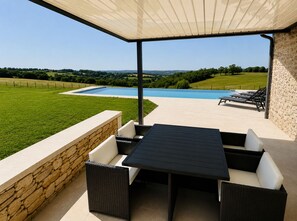 A covered outdoor seating area with a pool in the background. - Le Belvédère du Quercy - Domaine Gouloumès (Soucirac)