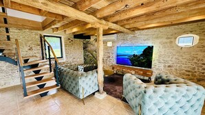 A spacious living area with a stone wall, a wooden staircase, and a large flat-screen TV. - Le Belvédère du Quercy - Domaine Gouloumès (Soucirac)
