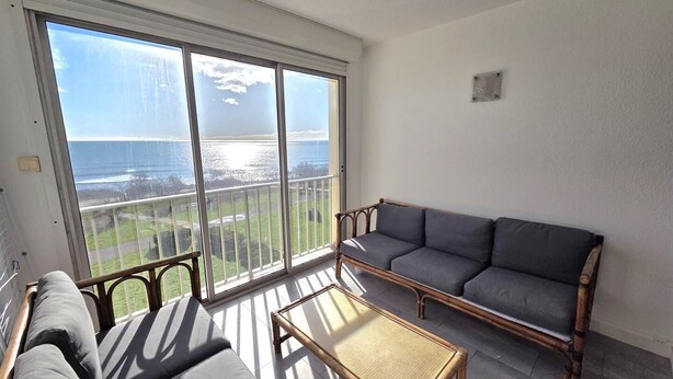 A balcony with a view of the ocean, a sofa, a chair, and a small table. - CAP D'AGDE - Plage du Môle // Réf 0208 (CAP D'AGDE)