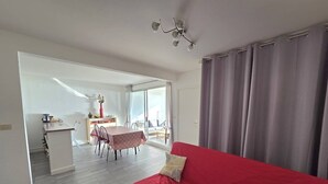 A modern living room with a red sofa, a dining area with a table and chairs, and a kitchen area with a counter and cabinets. - CAP D'AGDE - Plage du Môle // Réf 0208 (CAP D'AGDE)