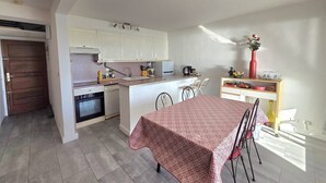 A compact kitchen with white cabinets, a dining table with a patterned tablecloth, and a small island with a vase. - CAP D'AGDE - Plage du Môle // Réf 0208 (CAP D'AGDE)