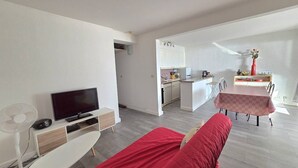 A modern living room with a TV, a red sofa, a dining table, and a kitchen in the background. - CAP D'AGDE - Plage du Môle // Réf 0208 (CAP D'AGDE)