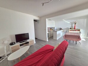 A modern living room with a TV, a red sofa, a dining table, and a kitchen in the background. - CAP D'AGDE - Plage du Môle // Réf 0208 (CAP D'AGDE)