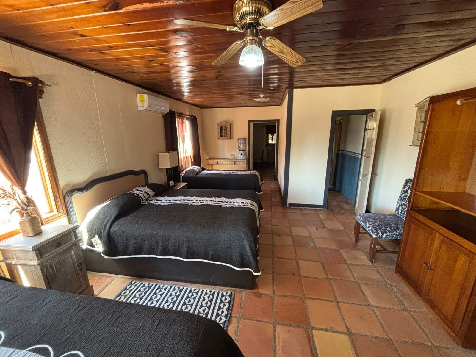 Ein Zimmer mit zwei Betten, Holzboden, Deckenventilator, Schreibtisch mit Lampe und Stuhl.