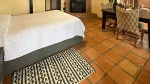 A room with a bed, a fireplace, a dining table with chairs, and a ceiling fan. - Hotel Molino Viejo  (San Quintín)