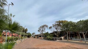 A dirt road leading to a building with a red roof, surrounded by trees and plants. - Hotel Molino Viejo  (San Quintín)