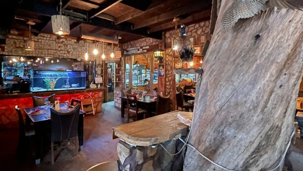 A rustic interior with exposed wooden beams, a stone wall, and a large wooden sculpture. - Hotel Molino Viejo  (San Quintín)