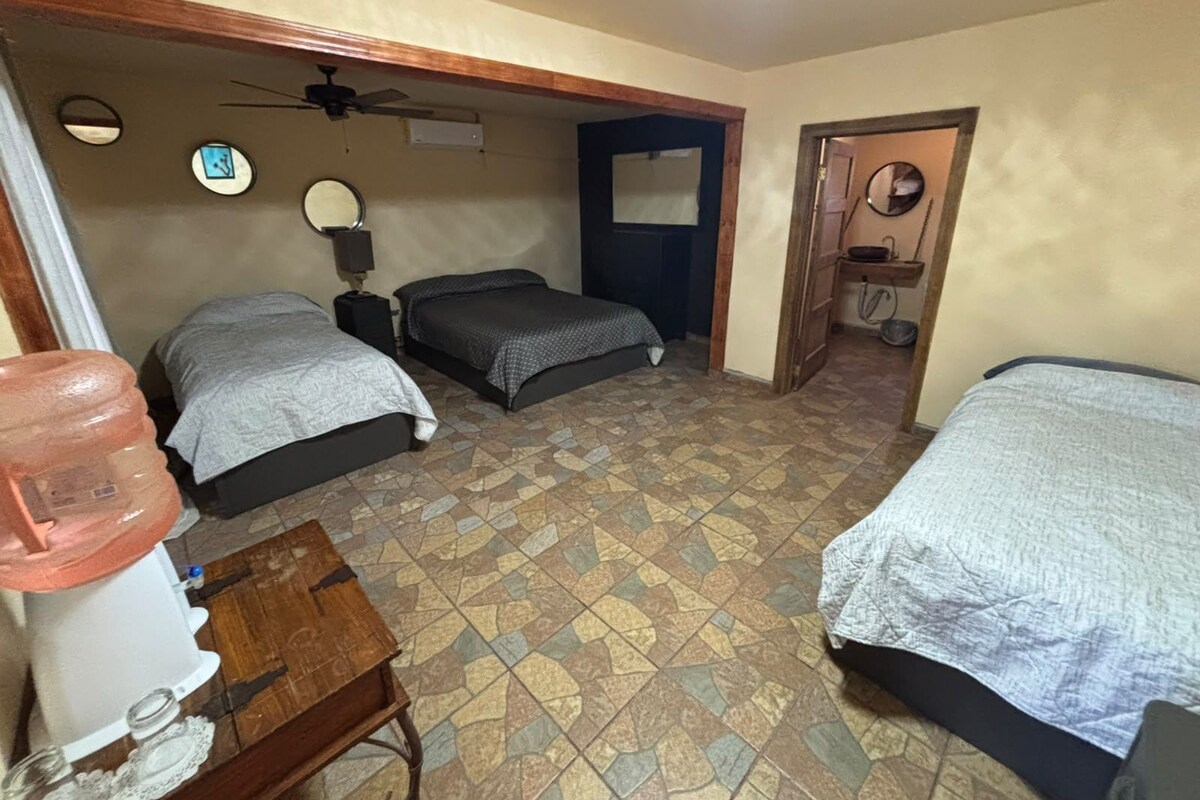 Une chambre avec deux lits, un ventilateur de plafond, un distributeur d’eau et une petite table.