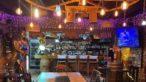 A bar with a stone wall, a wooden ceiling, and hanging light fixtures. - Hotel Molino Viejo  (San Quintín)