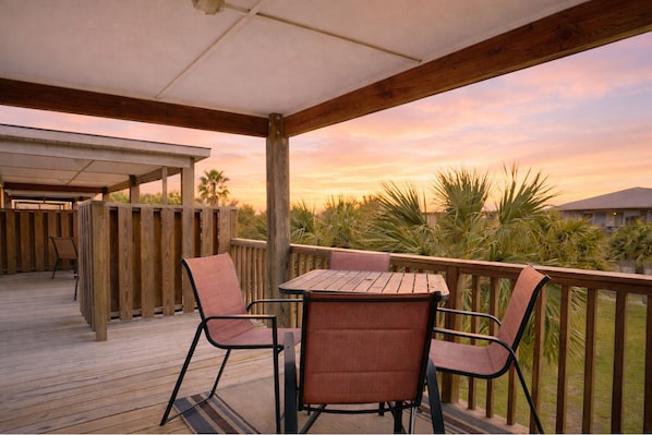 A wooden deck with a table and chairs, overlooking a landscaped area with palm trees. - LPC4A Shared Pool, Charcoal Grill, Garage Access, Boat Parking (Port Aransas)