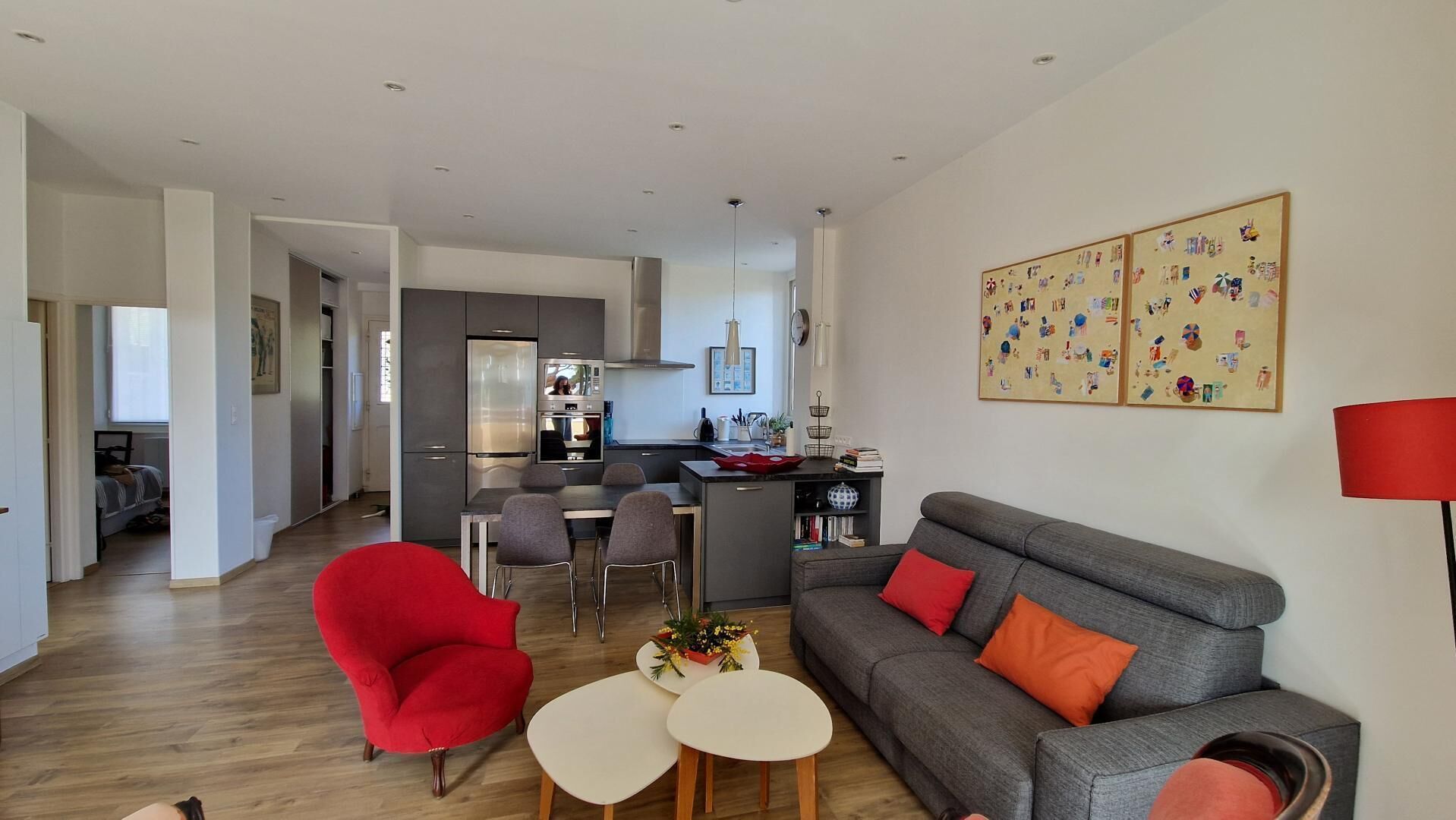 Um apartamento moderno com área de jantar, um sofá cinzento com almofadas vermelhas e uma poltrona vermelha, além de uma cozinha ao fundo.