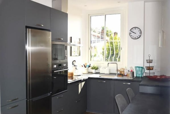 Una cocina moderna con un refrigerador de acero inoxidable, un microondas y un lavamanos. Hay una ventana que ofrece vistas a la vegetación.